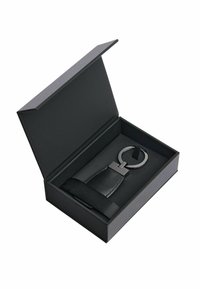 Black leather keychain holder with metallic loop and rectangular accent, presented in a sleek black box with a soft interior.