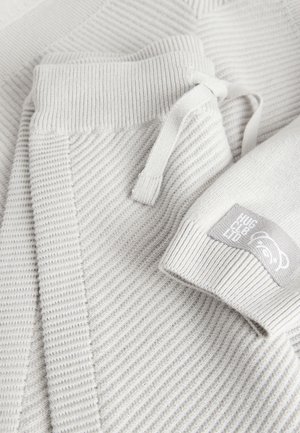 Light gray knit sweater featuring a ribbed texture, a drawstring at the waist, and a branded patch on the sleeve.