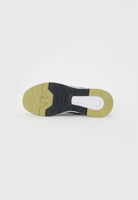 Shoe sole featuring a black rubber base with a yellow accent and textured grooves. White midsole section and logo detail embedded.