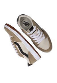 Zapatillas Vans con una combinación de colores beige, blanco y negro; material de ante y lona; suela plana; puntera redonda; cordones blancos; logo visible.