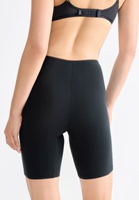 Schwarze, dehnbare, hochtaillierte Shorts mit glatter Textur, die bis zur Mitte des Oberschenkels reichen. Die Nähte am Saum und am Bund sind sichtbar.