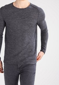 Pull à manches longues avec col rond en gris foncé, présentant un motif en maille texturée, des manches ajustées et une coupe décontractée.