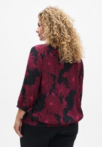 Blouse noire avec un motif floral en rose profond. Dotée de manches trois-quarts et d'une coupe décontractée, fabriquée dans un tissu léger.