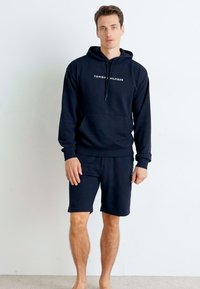 Sweat à capuche en coton bleu marine avec cordon de serrage et poche kangourou, associé à un short assorti. Présente le logo blanc "TOMMY HILFIGER" sur la poitrine.