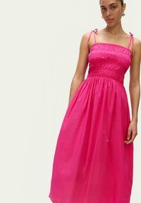 Abito lungo rosa con corpetto arricciato, spalline sottili regolabili e gonna fluente. Realizzato in tessuto leggero. Senza motivi o decorazioni.