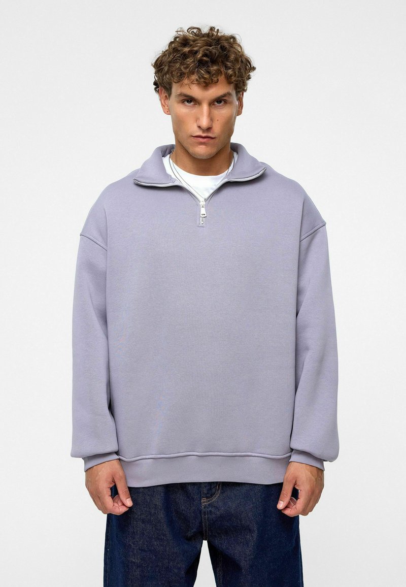 Lichtpaarse ritsvest met hoge kraag, ontspannen pasvorm en lange mouwen. Zachte stof en geribbelde zoomdetails. Draagt met donkere spijkerbroeken.