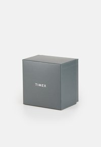 Caja de cartón gris con forma cuadrada, con un logo blanco de "TIMEX" en la parte frontal, textura suave y bordes limpios.