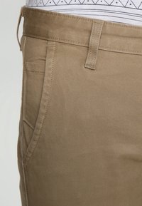 Pantaloni in cotone beige con una texture liscia, dotati di una vita standard, tasche laterali e dettagli di cucitura discreti.