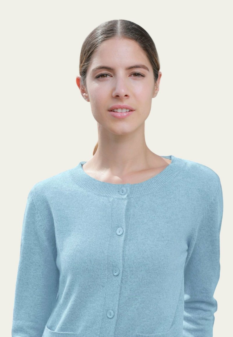Cardigan bleu clair en matière douce, avec un col rond, une fermeture à boutons et deux poches. Tissu texturé au design classique.