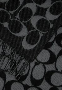 Juoda ir pilka skara, puošta geometriniu persidengusių ratų raštu, su kutais viename krašte ir minkšta, tekstūruota medžiaga.