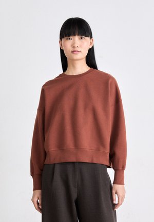 Brauner, kurzer Sweatshirt mit langen Ärmeln, aus weichem Stoff gefertigt. Verfügt über einen runden Halsausschnitt und leicht gesenkte Schulternähte.