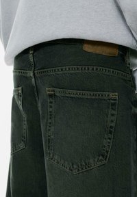 Lähikuva mustista denimpöksyistä, mille on nähtav stitching ja osaliselt halli dressipluus katab vöökoha ala.