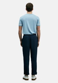Lichtblauw t-shirt met korte mouwen en witte strepen bij de mouwen, gecombineerd met donkerblauwe tapered broeken met achterzakken, en witte sneakers.