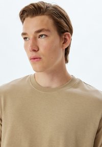 Beige sweatshirt med rund hals lavet af glat bomuldsblandingsstof, med ribbet krave og sømløse skuldre for et rent udseende.
