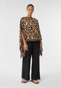 Wzorzysty poncho w geometryczny brązowy, pomarańczowy i kremowy wzór. Połączone z czarnymi szerokimi spodniami i sandałami z złotymi akcentami.