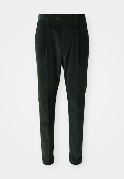 Mørkegrønne kordfløjl bukser med bæltestropper, frontknap, plissee, indsnævrede ben og manchetter på en hvid baggrund.