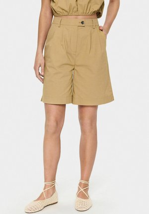 Shorts haut de taille en khaki avec des plis, des poches latérales et une fermeture à bouton. Tissu lisse avec un léger éclat, présentant une coupe décontractée.