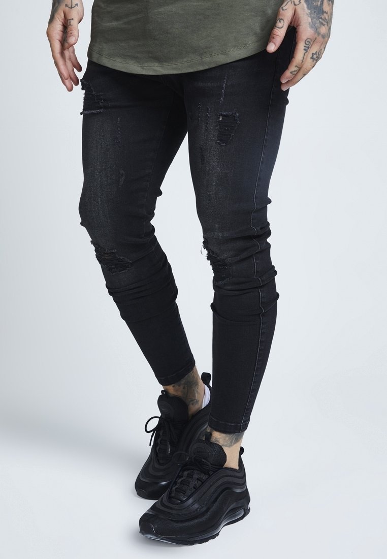 Svarta slitna skinny jeans med flera hål och urtvättning. Matchas med svarta sneakers, som har en slät yta och texturerade detaljer.