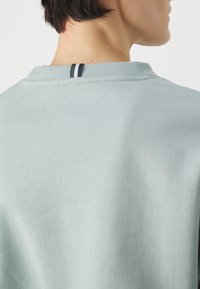 Felpa azzurra chiara con tessuto strutturato, colletto rotondo e un accento a righe verde, blu navy e bianco sul retro del collo.