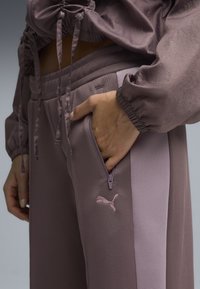 Fioletowy dres z teksturowaną górą i gładkimi spodniami z haftowanym logo. Zawiera kieszenie na zamek błyskawiczny i regulowane sznurki.