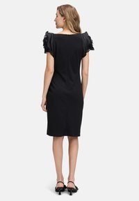 Schwarzes Kleid mit kurzen, gerafften, durchsichtigen Ärmeln, gerader Passform und einem Reißverschluss auf der Rückseite. Knielang mit glatter Textur und minimaler Gestaltung.
