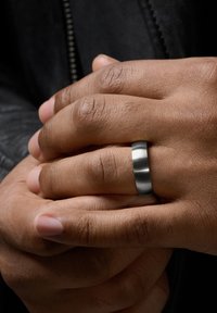 Matte gray metal ring on fingers slightly overlapping, showcasing smooth texture and wide band against the skin's natural tones.