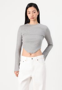 Haut cropped à manches longues côtelé gris avec un ourlet arrondi, associé à un jean blanc taille haute, présentant une texture subtile et un design ajusté.