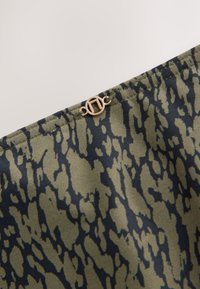 Gros plan sur un tissu à motif abstrait vert et noir avec une petite boucle ronde en métal doré attachée près du bord.