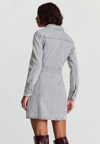 Abito in denim grigio con maniche lunghe, collo con rever e vita con cintura. Presenta dettagli con bottoni sul davanti e una silhouette svasata aderente.