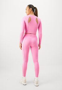 Haut rose ajusté à manches longues avec un dos découpé, associé à un legging taille haute assorti avec des coutures accentuées.