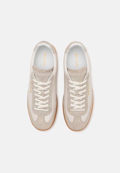 Beež nahk- ja suedesneakers valgete paeltega, tekstuursete detailidega ja kummist tallaga. Omab kuldset logo keeles.