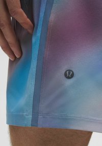 Pantalones cortos deportivos para hombre en tonos degradados de azul y morado. Fabricados con material suave y ligero, cuentan con un parche de logo y una costura lateral en contraste.