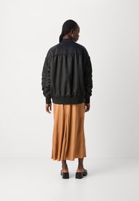 Schwarze Bomberjacke mit gesteppten Ärmeln, gerippten Bündchen und Kragen, kombiniert mit einem orangen Midikleid. Glatte Textur, lässiges Design.