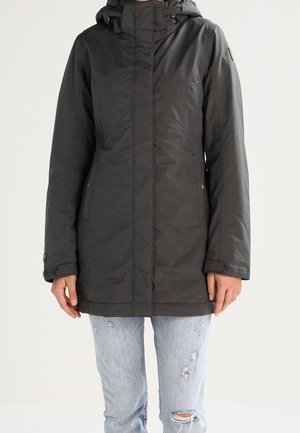 Mørk grå lang frakke med hætte, lynlås fortil og sidelommer. Har en glat tekstur og let glans, parret med slidte jeans.