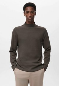 Suéter de cuello alto ligero y marrón con mangas largas, textura suave y diseño ajustado, combinado con pantalones de color claro.