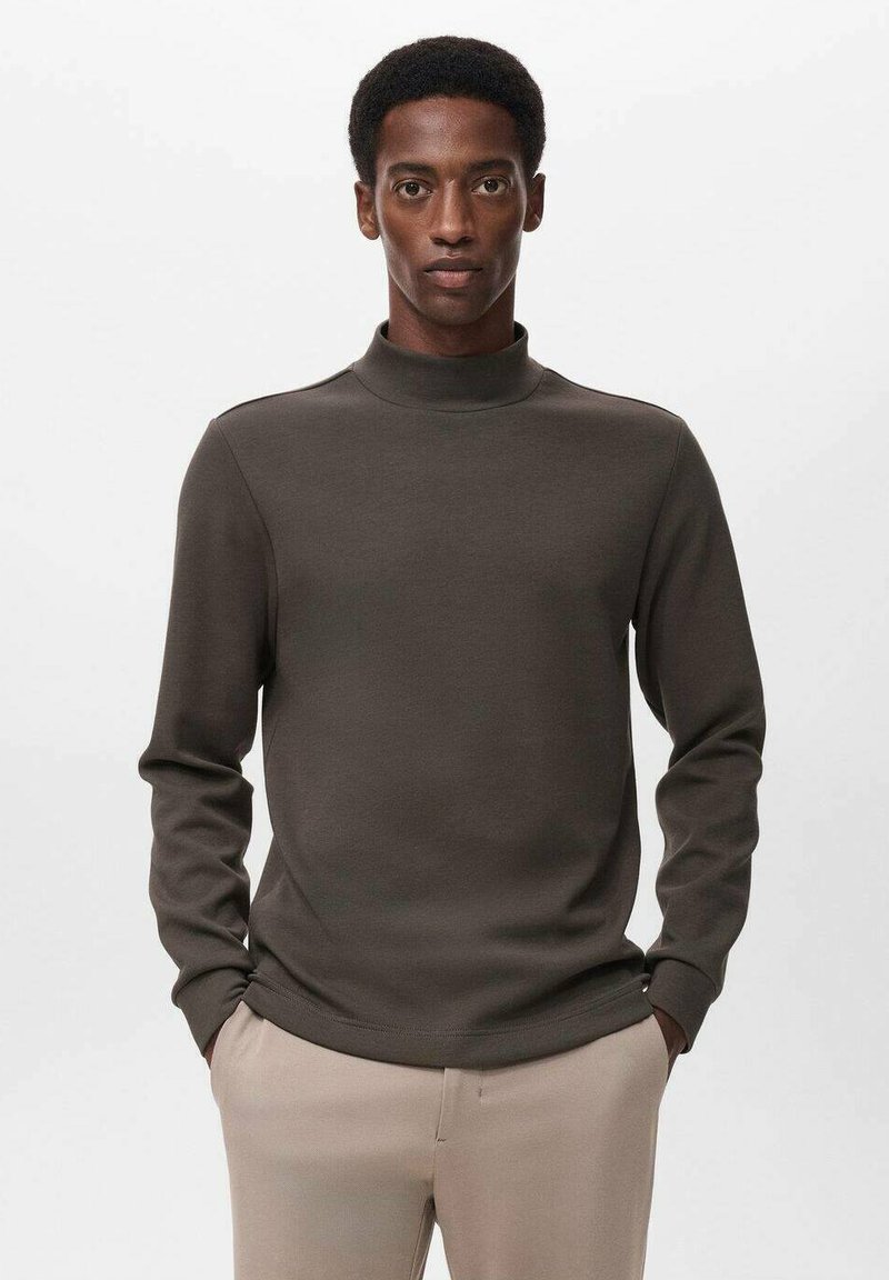 Suéter de cuello alto ligero y marrón con mangas largas, textura suave y diseño ajustado, combinado con pantalones de color claro.