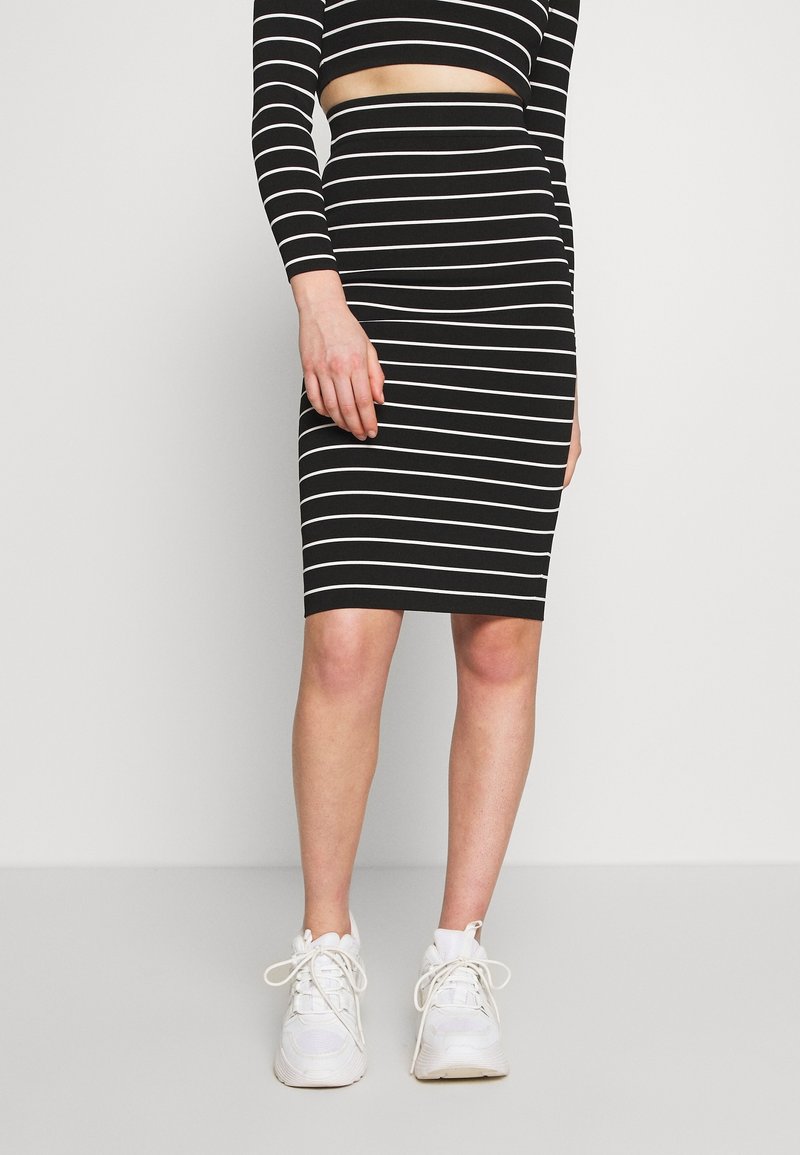 Vestido bodycon de rayas blancas y negras con mangas largas y una sección media recortada, combinado con zapatillas blancas. Textura suave.