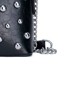 Bolso de mano de piel sintética negra con tachuelas metálicas plateadas, correa de cadena y forma rectangular. Superficie texturada con un acabado brillante.