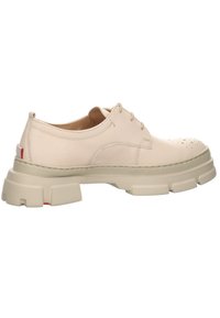 Chaussure oxford en cuir beige avec semelle épaisse texturée, fermeture à lacets à l'avant, bout perforé et détail rouge subtil sur la languette du talon.