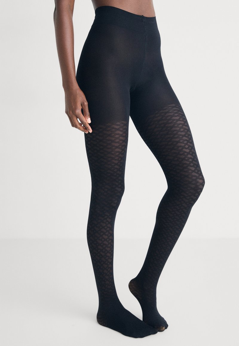 Pantys negras con un diseño estampado, con una sección superior transparente y un diseño de diamante texturizado en las piernas inferiores. Fabricadas con material elástico.