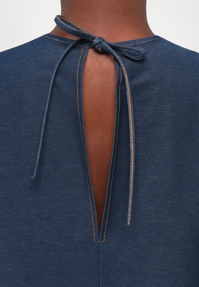 Tumši zilas krāsas apģērbs ar atslēgvietu aizmugurē, sasiets pie kakla ar atbilstošu audumu. Malas rotā kontrastējoša oranža dūriens.