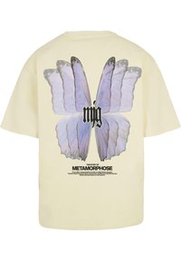 Lyst beige t-shirt med et stort blåt sommerfugle-motiv på ryggen, med sort tekst nedenunder der står "METAMORPHOSE'S HISTORIE."