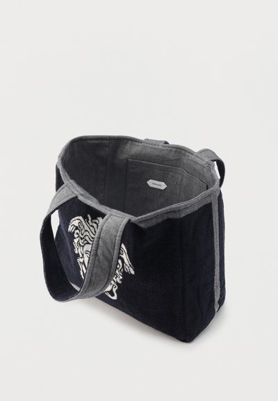Μαύρη και γκρι υφασμάτινη τσάντα ώμου με φαρδιές τιράντες, ανοιχτό πάνω μέρος, εσωτερική τσέπη και λευκό κεντητό σχέδιο κεφαλής Μέδουσας στο πλάι.