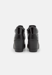 Scarpe nere con tacco alto, finitura lucida in vernice, punta rotonda, collo imbottito e cerniera laterale per una facile calzata. Tacco a cuneo strutturato.