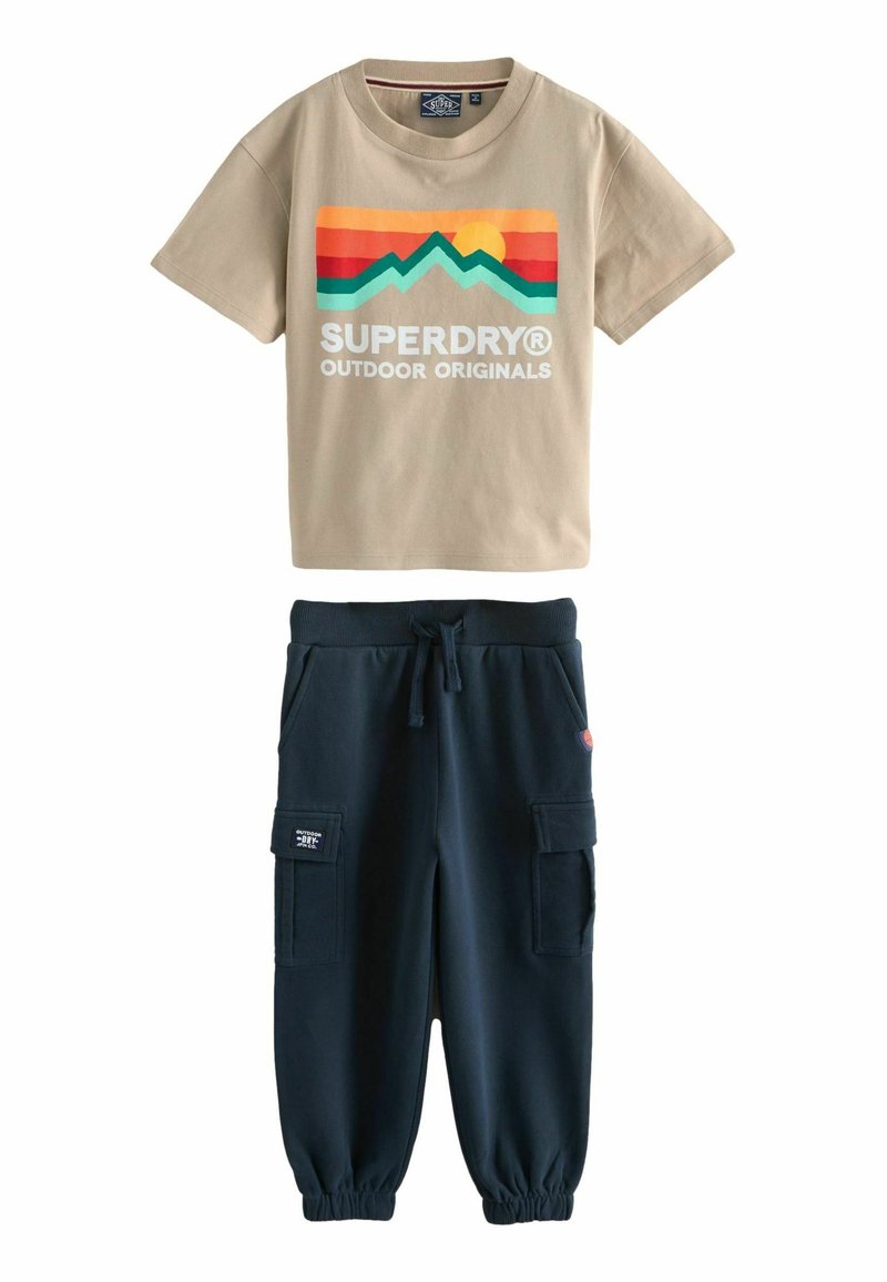 Béžové bavlněné tričko s barevnou grafikou hor a logem. Námořnické joggingové kalhoty s elastickými manžetami, pasem a bočními kapsami.