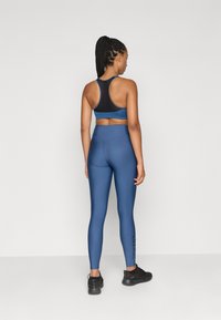 Ναυτικό αθλητικό σουτιέν με σχέδιο racerback και λεπτομέρειες από δικτυωτό ύφασμα, σε συνδυασμό με ψηλόμεσα μπλε κολάν που διαθέτουν λογότυπο στο αριστερό πόδι.