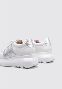 Zapatillas blancas con detalles plateados, cuero texturizado y una gruesa suela blanca con un patrón en zigzag. Diseño de cordones y cuello acolchado.