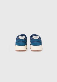 Pair of blue Saucony sneakers viewed from the back, featuring white midsoles and brown rubber outsoles on a plain background.