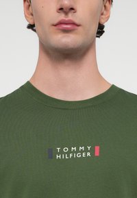 Πράσινο βαμβακερό μπλουζάκι με στρογγυλή λαιμόκοψη. Διαθέτει bold λογότυπο "TOMMY HILFIGER" σε λευκό, ναυτικό και κόκκινο χρώμα, το οποίο είναι κεντρικά τοποθετημένο στο στήθος.