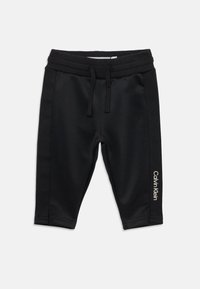 Čierne športové šortky vyrobené z hladkej tkaniny, s elastickým pásom so šnúrkou a bielym logom „Calvin Klein“ na strane.